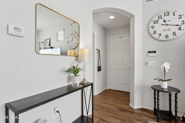 corridor featuring arched walkways, visible vents, baseboards, and dark wood-style flooring