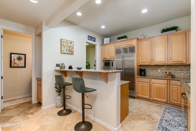 kitchen featuring a breakfast bar, backsplash, built in appliances, light stone countertops, and light brown cabinets