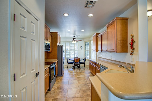 kitchen with a textured ceiling, stainless steel appliances, sink, kitchen peninsula, and ceiling fan