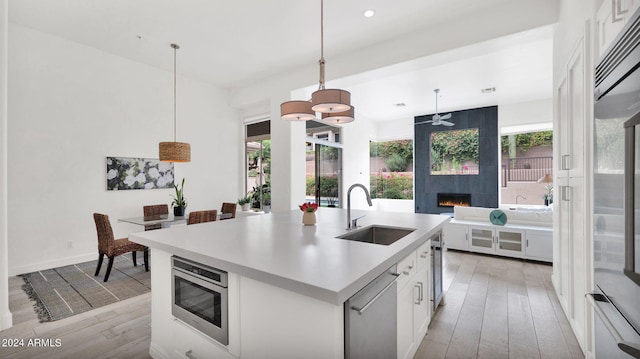 kitchen with light wood finished floors, built in appliances, a fireplace, and a sink