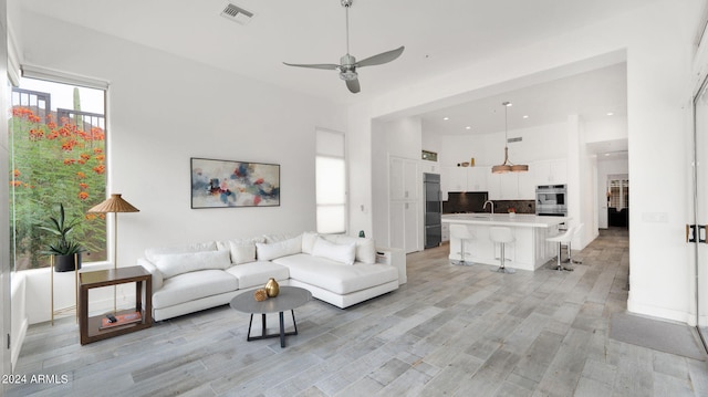 living area featuring visible vents, a towering ceiling, recessed lighting, light wood-style floors, and ceiling fan