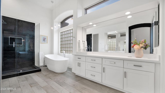 bathroom featuring a freestanding bath, a stall shower, a high ceiling, wood finished floors, and vanity