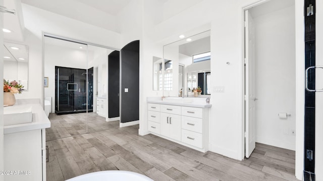 bathroom with a shower stall, two vanities, baseboards, and wood finished floors