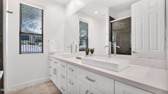 bathroom with a sink, wood finished floors, a stall shower, and double vanity