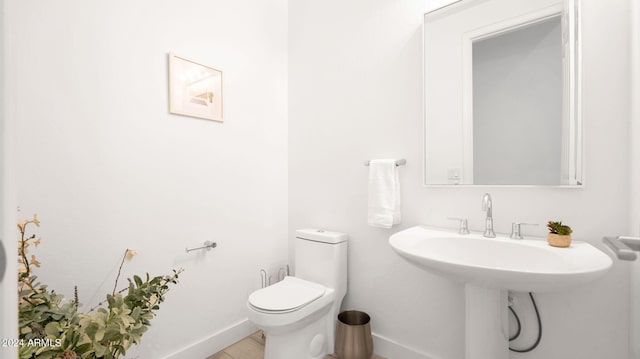 half bath featuring toilet, baseboards, and a sink