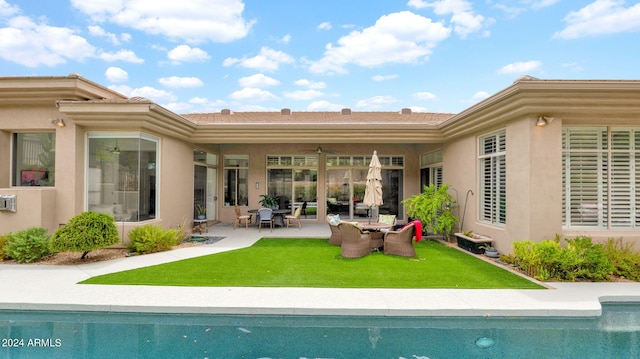 rear view of property with a patio area, a lawn, an outdoor pool, and a ceiling fan