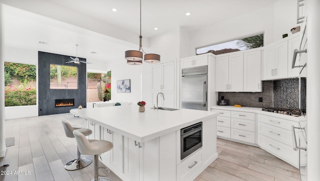 kitchen with backsplash, built in appliances, a fireplace, light wood-style floors, and a sink