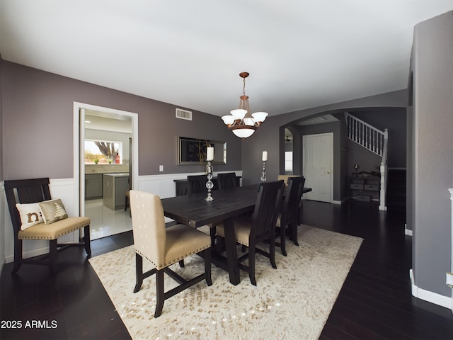 dining area featuring arched walkways, dark wood-style flooring, visible vents, stairway, and wainscoting