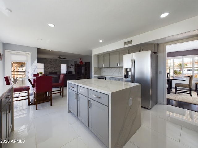 kitchen with light stone counters, a center island, gray cabinetry, a fireplace, and stainless steel refrigerator with ice dispenser