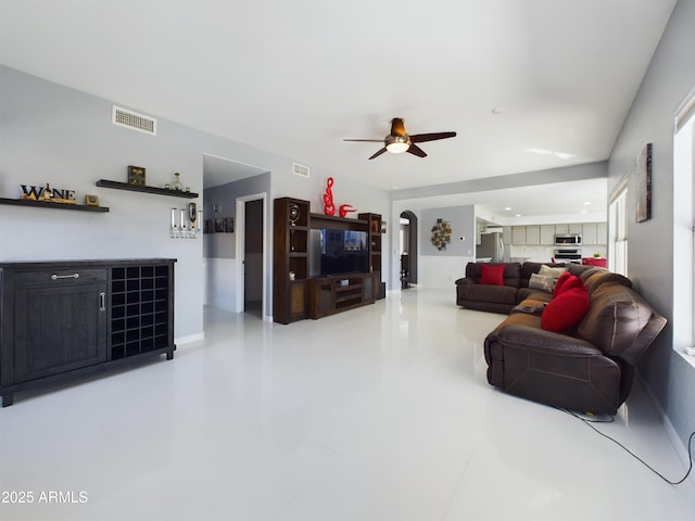 living area featuring a dry bar, ceiling fan, visible vents, and arched walkways