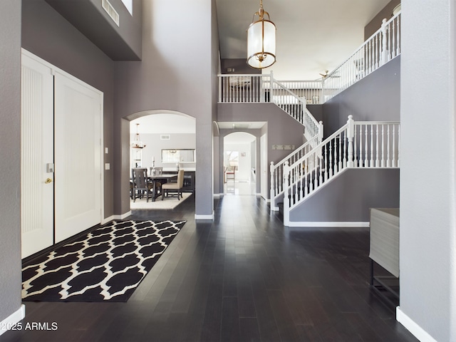 entrance foyer featuring a towering ceiling, stairs, arched walkways, and dark wood-style flooring