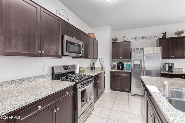 kitchen with appliances with stainless steel finishes, dark brown cabinetry, light stone counters, and light tile patterned floors