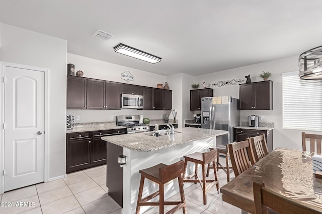 kitchen featuring a center island with sink, sink, light tile patterned flooring, dark brown cabinetry, and stainless steel appliances