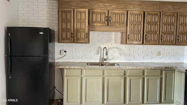 kitchen featuring a sink, tasteful backsplash, freestanding refrigerator, and light stone counters