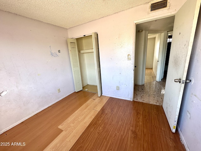 unfurnished bedroom with visible vents, a closet, a textured ceiling, and wood finished floors