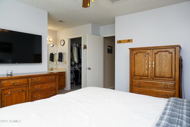 bedroom with ensuite bath, a textured ceiling, ceiling fan, a spacious closet, and a closet