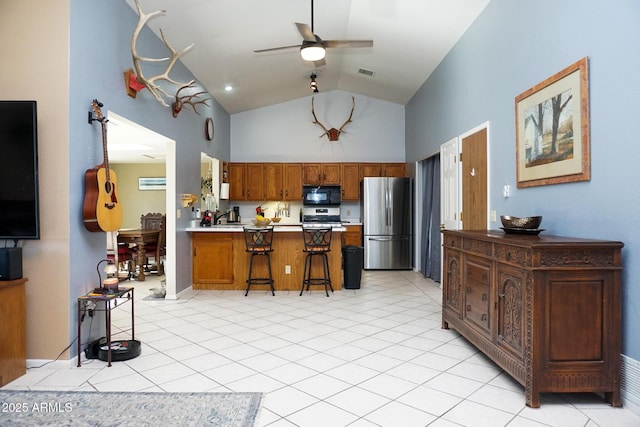 kitchen with stainless steel refrigerator, ceiling fan, a kitchen breakfast bar, light tile patterned floors, and range