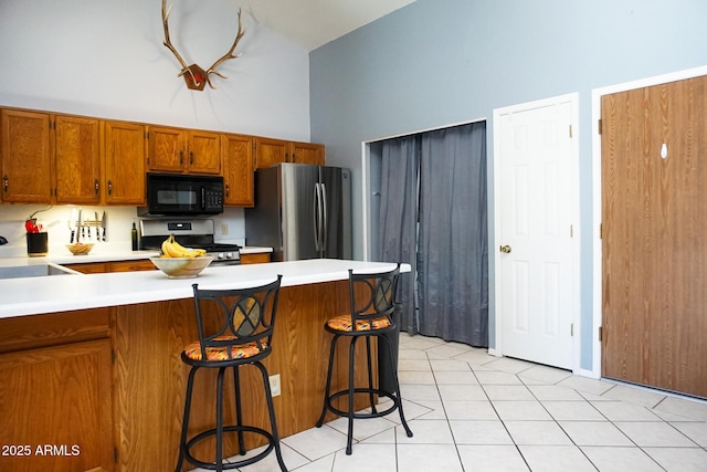 kitchen featuring a high ceiling, sink, light tile patterned floors, a kitchen bar, and stainless steel appliances