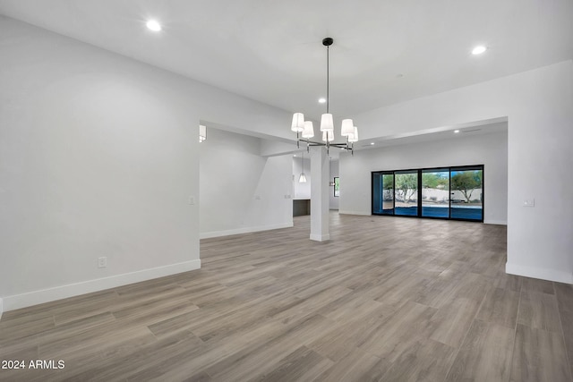 unfurnished living room with an inviting chandelier and light hardwood / wood-style floors