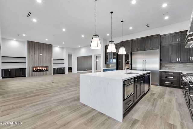 kitchen featuring tasteful backsplash, a kitchen island with sink, light hardwood / wood-style flooring, and decorative light fixtures