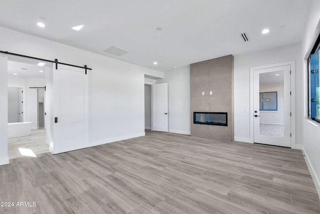 unfurnished living room featuring light hardwood / wood-style flooring, a fireplace, and a barn door