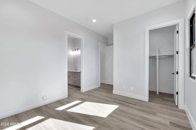 unfurnished bedroom featuring sink, a walk in closet, ensuite bath, a closet, and light hardwood / wood-style floors