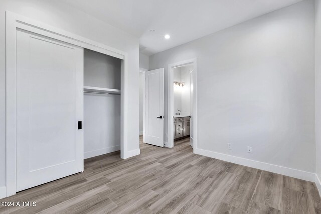 unfurnished bedroom with ensuite bath, light hardwood / wood-style floors, and a closet