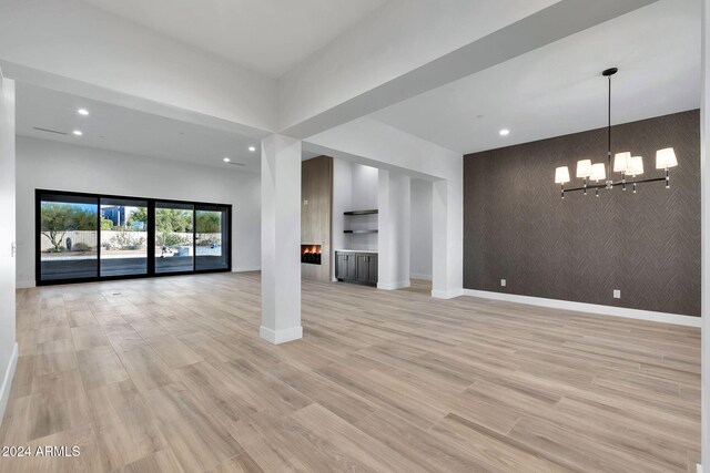 unfurnished living room featuring an inviting chandelier and light hardwood / wood-style floors