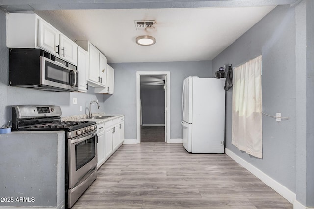 3913 W Sherman St, Phoenix, AZ 85009 - kitchen with stainless steel appliances, white cabinetry, baseboards, and light wood-type flooring