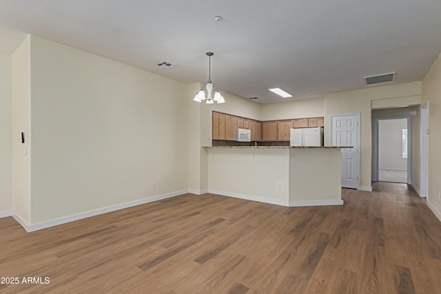 kitchen featuring a peninsula, white appliances, visible vents, and brown cabinets