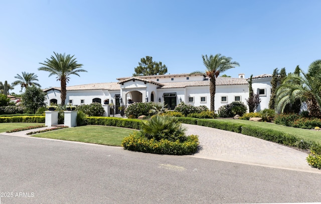 mediterranean / spanish home featuring stucco siding, fence, a front lawn, and a tile roof