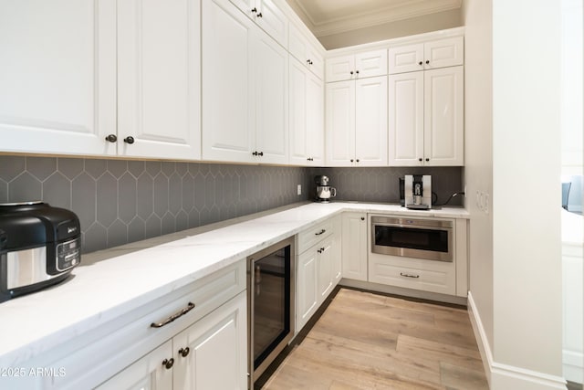 kitchen featuring crown molding, built in microwave, wine cooler, decorative backsplash, and white cabinets