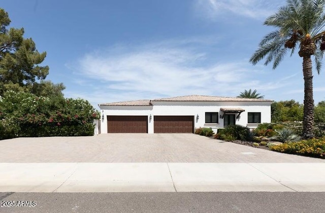 mediterranean / spanish home featuring a tile roof, a garage, driveway, and stucco siding