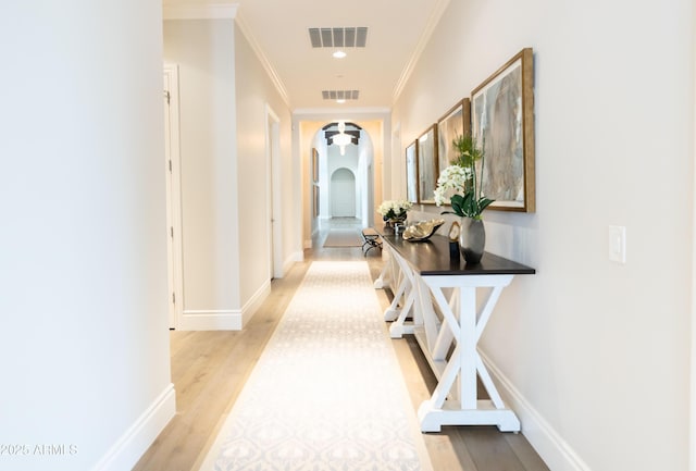 hallway with light wood-type flooring, visible vents, arched walkways, and crown molding