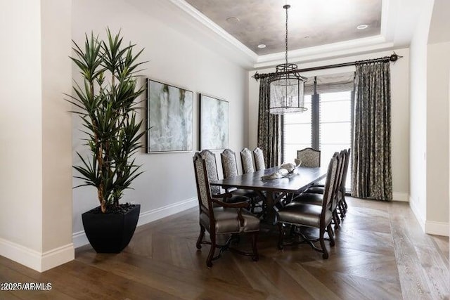 dining area featuring an inviting chandelier, a raised ceiling, crown molding, and baseboards