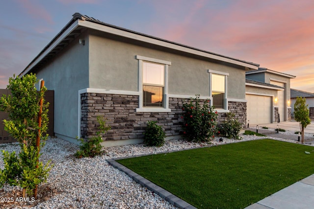 18139 W Oregon Ct, Litchfield Park, AZ 85340 - property exterior at dusk featuring stone siding, stucco siding, an attached garage, a lawn, and concrete driveway