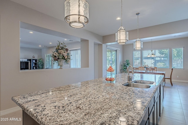 kitchen featuring sink, hanging light fixtures, a kitchen island with sink, light tile patterned floors, and light stone countertops