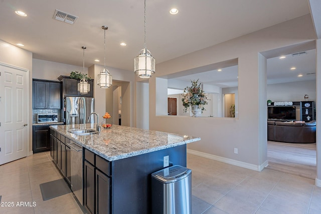 kitchen featuring sink, hanging light fixtures, stainless steel appliances, light stone counters, and a center island with sink