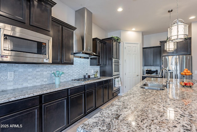 kitchen featuring wall chimney exhaust hood, sink, hanging light fixtures, appliances with stainless steel finishes, and backsplash