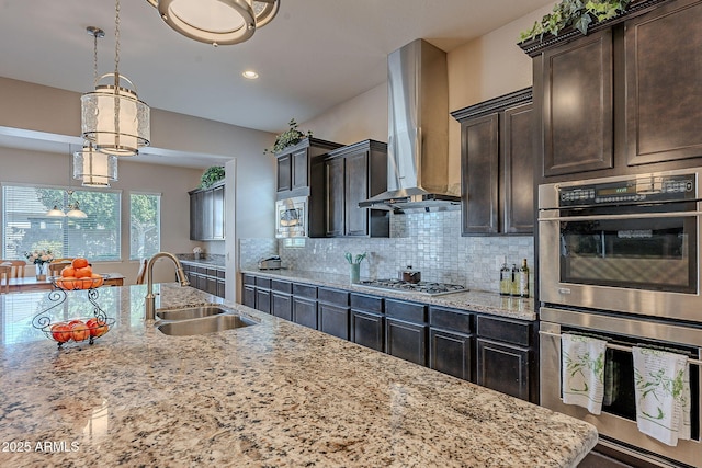 kitchen with pendant lighting, sink, stainless steel appliances, dark brown cabinetry, and wall chimney exhaust hood