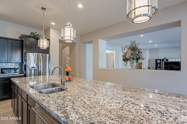 kitchen with decorative light fixtures, sink, stainless steel fridge, decorative backsplash, and light stone counters