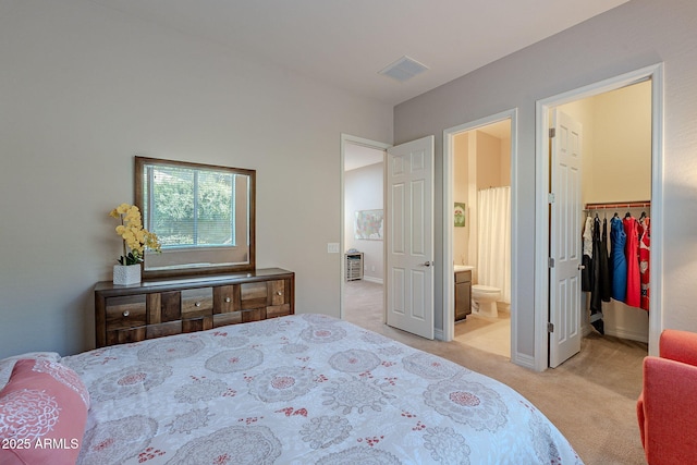 bedroom with connected bathroom, a walk in closet, light colored carpet, and a closet