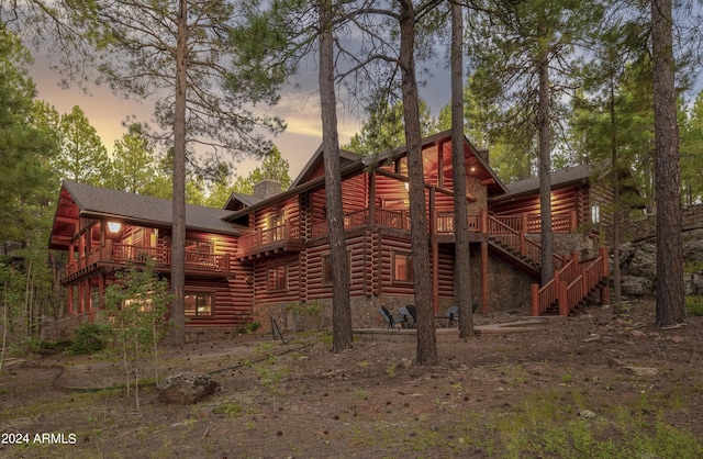 back of property at dusk featuring log siding, stairway, a chimney, and a wooden deck