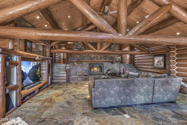 unfurnished living room with a fireplace, high vaulted ceiling, beamed ceiling, rustic walls, and ceiling fan