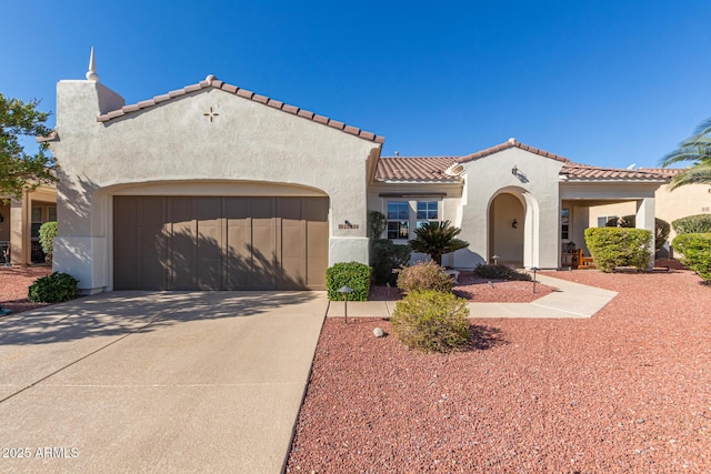 mediterranean / spanish-style house featuring a garage, concrete driveway, a tiled roof, and stucco siding