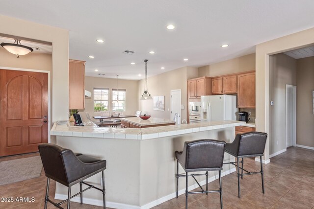 kitchen featuring tile countertops, white appliances, a breakfast bar area, and visible vents