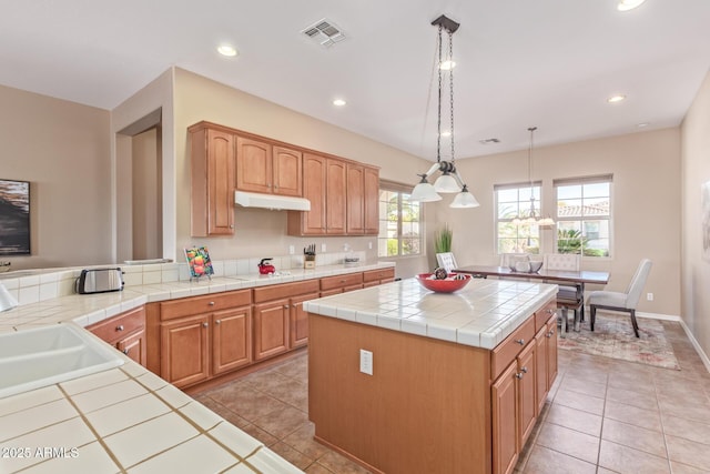 kitchen featuring light tile patterned floors, visible vents, tile countertops, a kitchen island, and under cabinet range hood