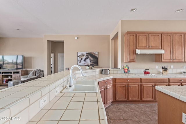 kitchen with light tile patterned floors, tile countertops, open floor plan, under cabinet range hood, and a sink