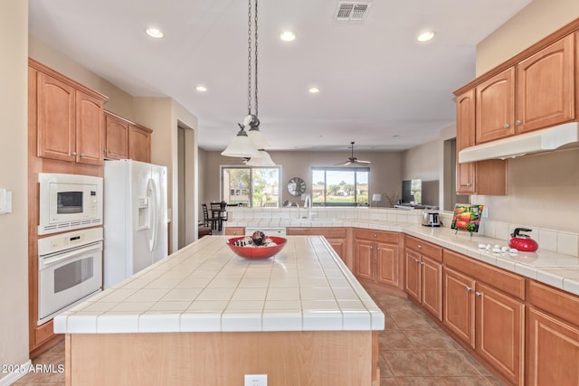 kitchen featuring a peninsula, white appliances, a kitchen island, a sink, and visible vents