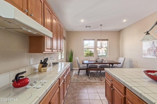 kitchen featuring tile countertops, brown cabinetry, visible vents, and under cabinet range hood